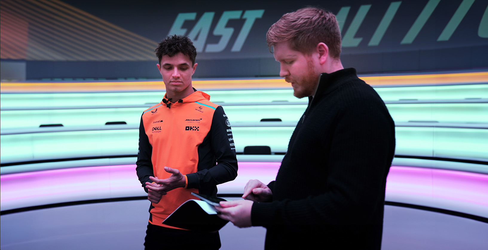 Joe Durr and Lando Norris in a studio with colorful curved LED lights in the background.